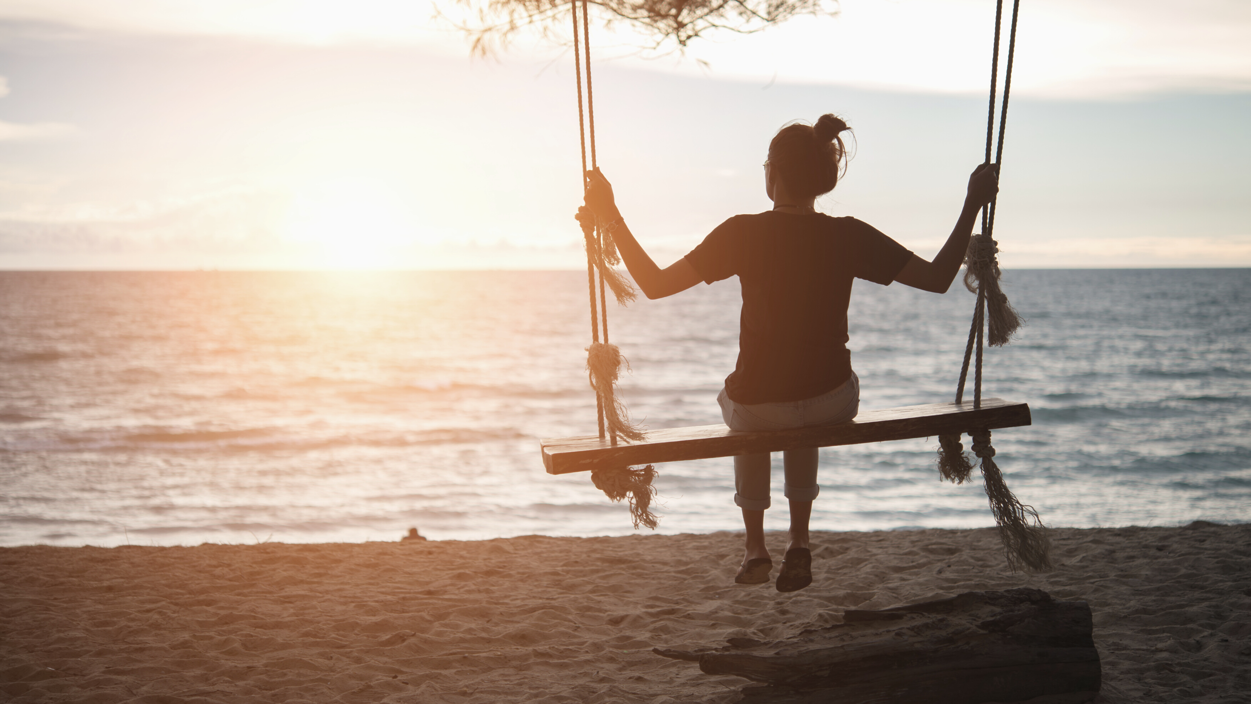 woman swinging by the beach at sunset