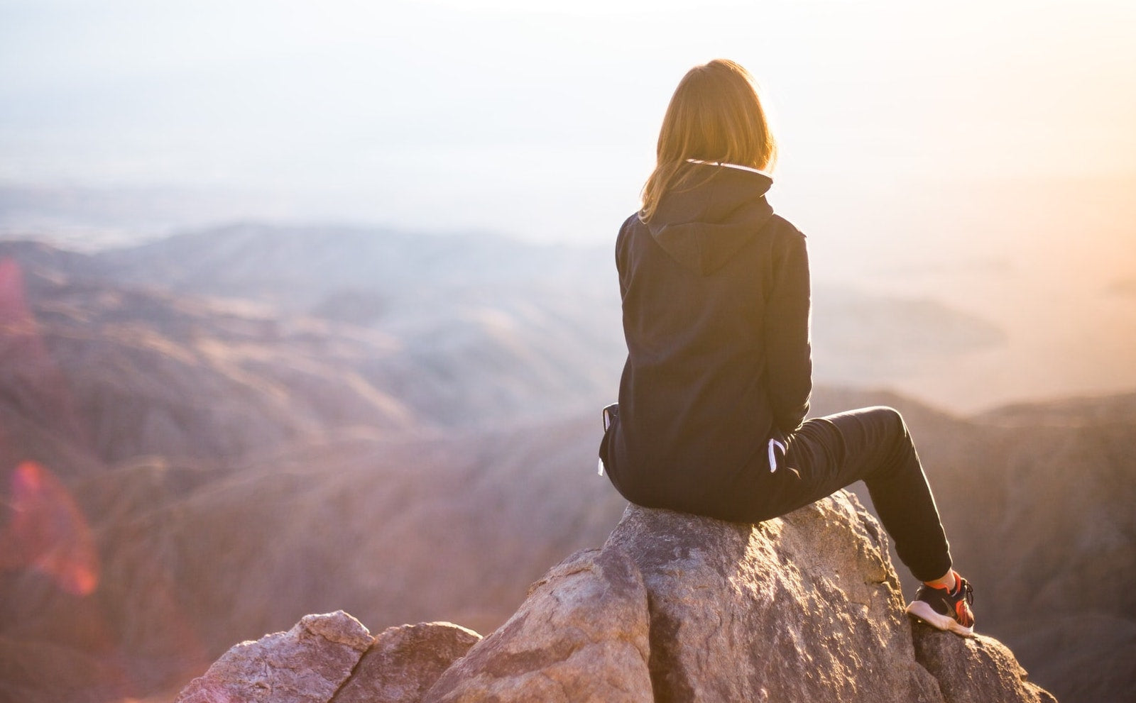 woman wearing a black jacket sitting on rocks looking at mountains