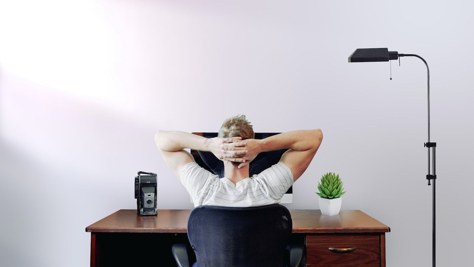 Man at desk in front of computer with hands behind his head