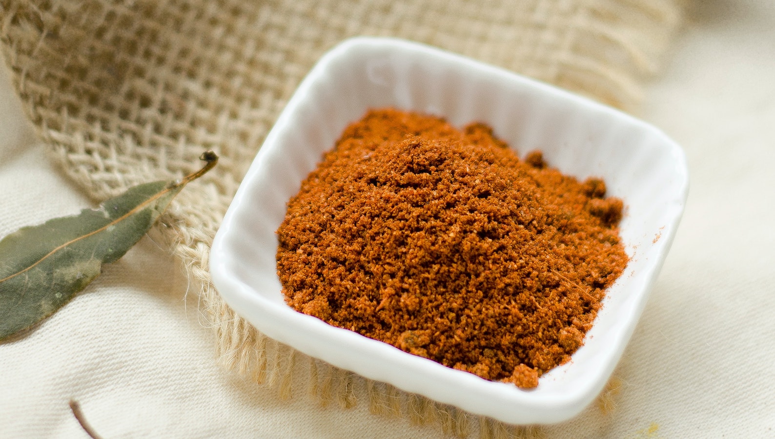 Ground cinnamon in white cup on weaved cloth