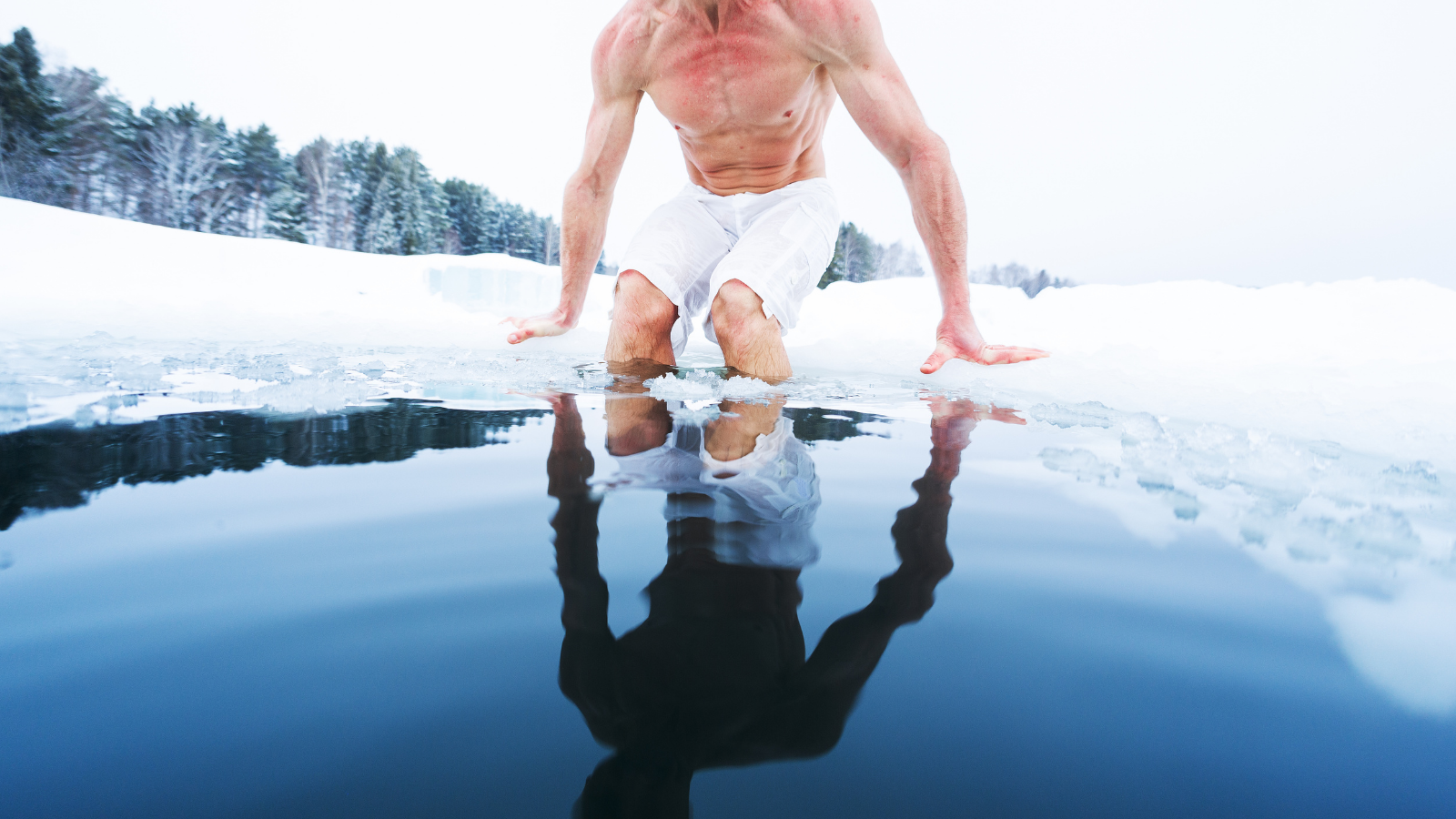 Shirtless man getting into icy pool surrounded by snow