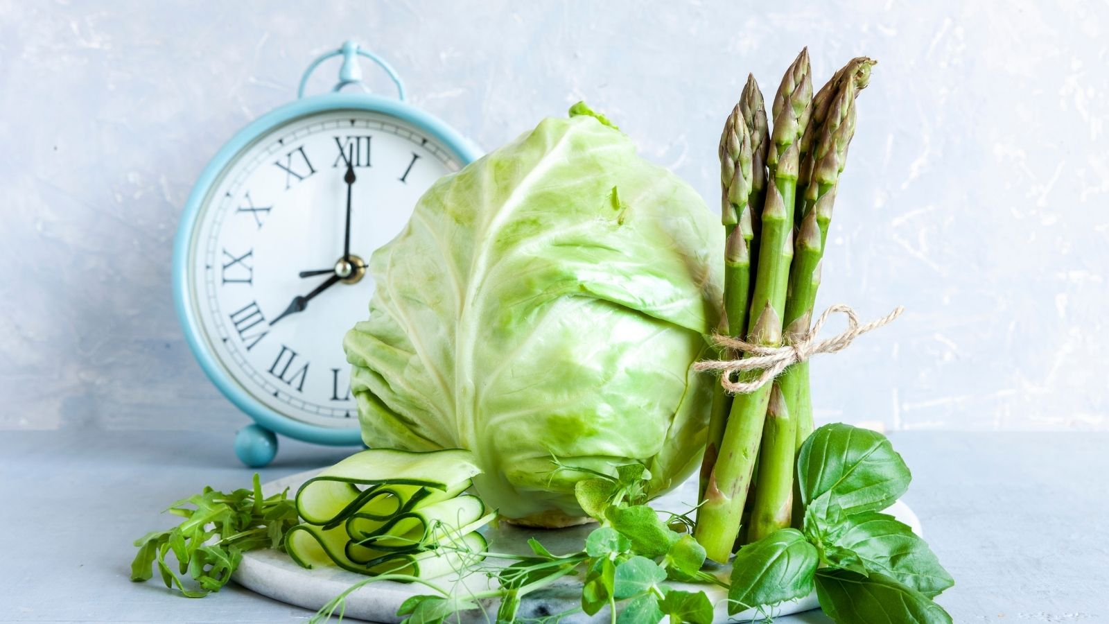 Clock behind green vegetables on a gray background