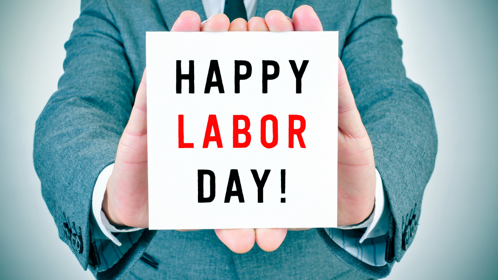 Man in suit holding white sign that says 'Happy Labor Day'.
