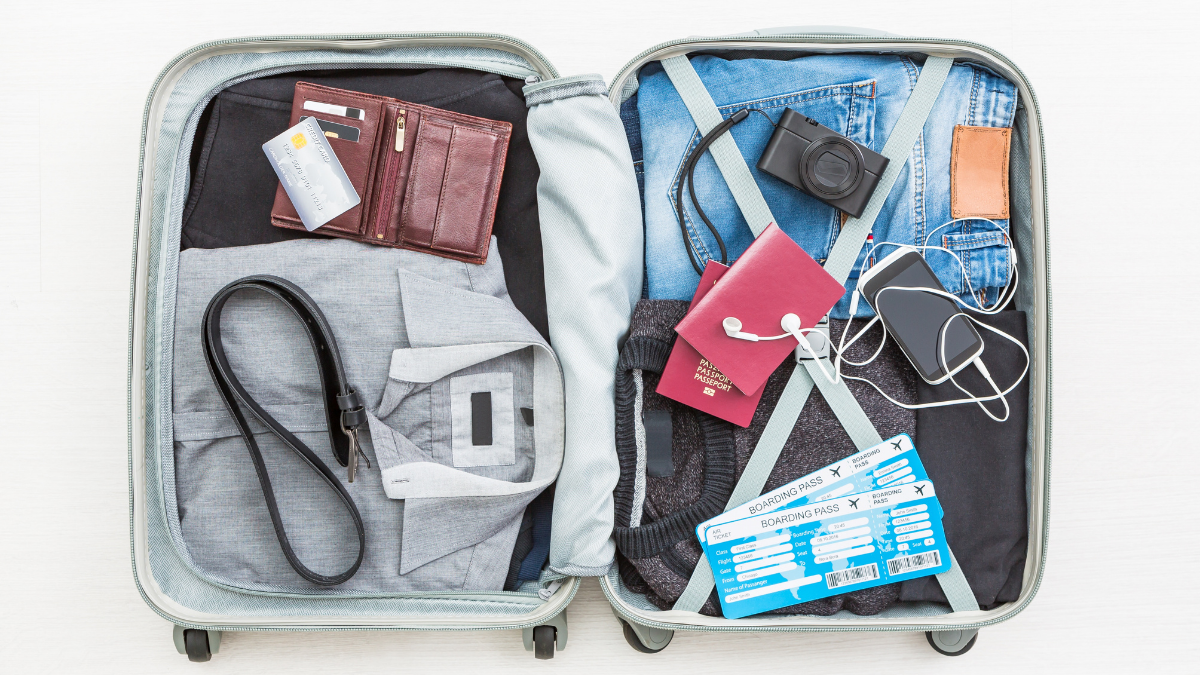 Open suitcase containing wallet, clothes, passport, boarding pass, and camera