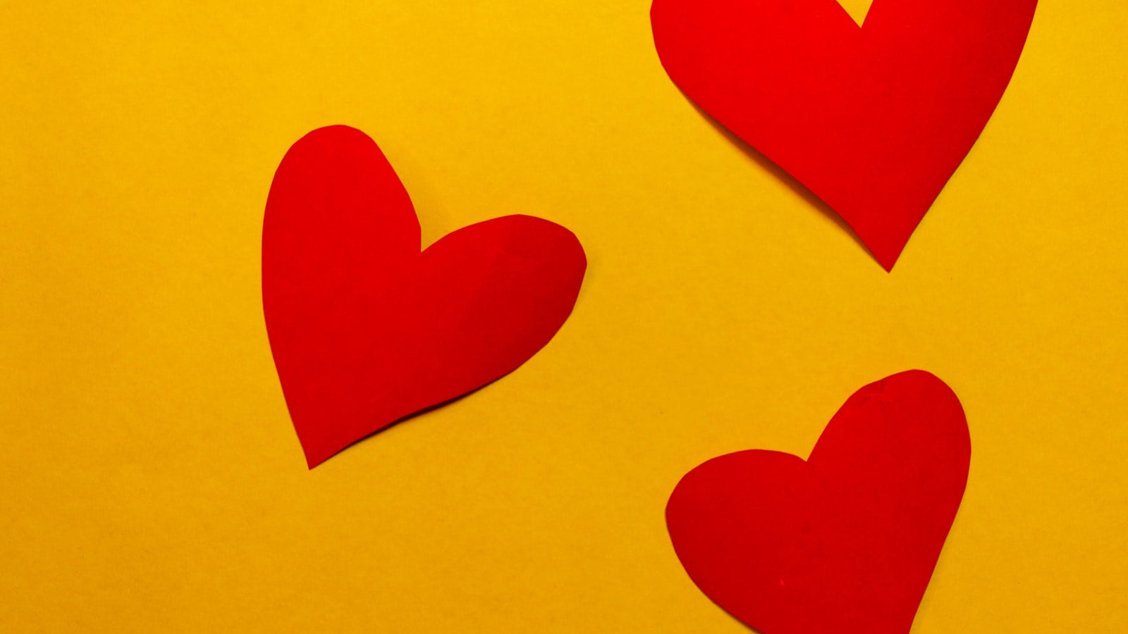 three red paper hearts against yellow background