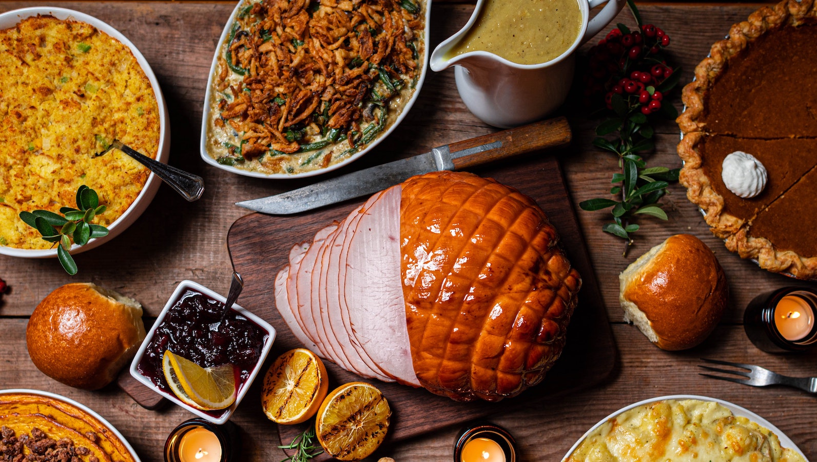 Thanksgiving dinner with ham, pumpkin pie, cranberry sauce, bread, and casserole on a wooden table 